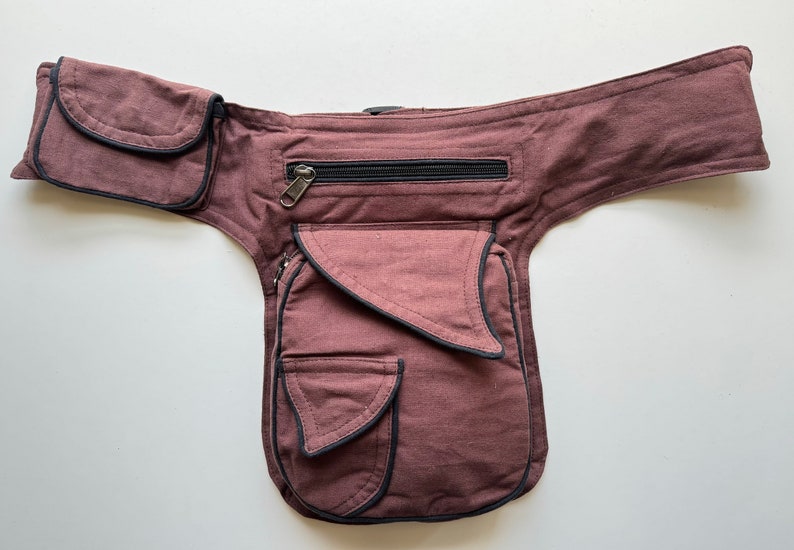 May include: A brown canvas fanny pack with multiple pockets and a zippered compartment. The pack has black trim around the edges.