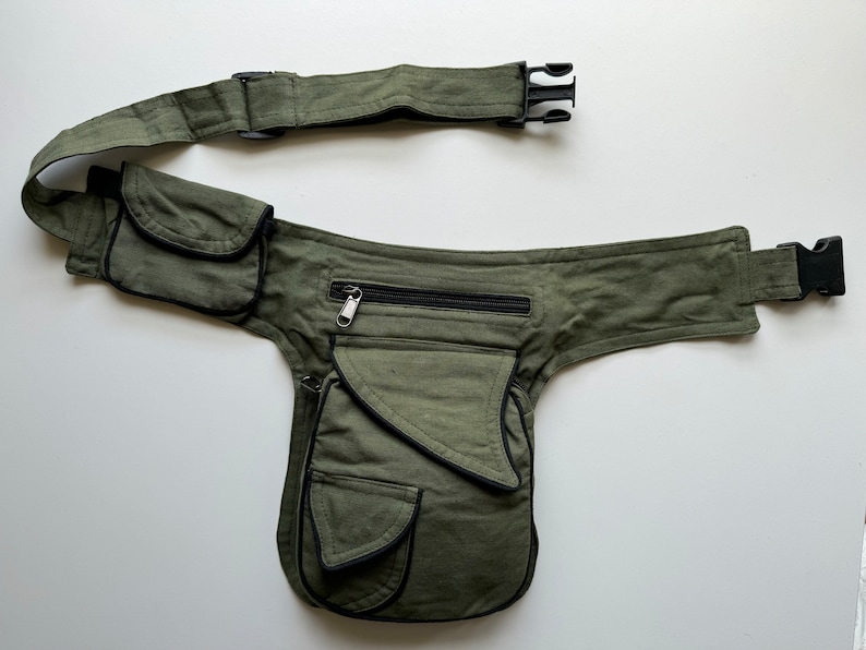 May include: A green canvas fanny pack with multiple pockets and a black zipper. The fanny pack has a black adjustable strap with a plastic buckle.
