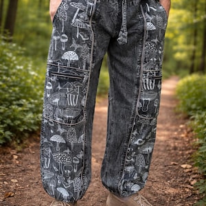 May include: Dark grey trousers with a white mushroom pattern. The trousers have a drawstring waist, pockets, and are cuffed at the ankles. The person in the image is wearing brown shoes.