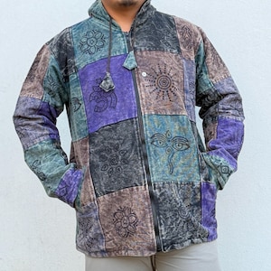 Puede incluir: Una sudadera con cremallera de patchwork en tonos morado, verde azulado, marrón y negro. La chaqueta tiene capucha, cremallera completa y bolsillos. El diseño incluye varios símbolos espirituales.