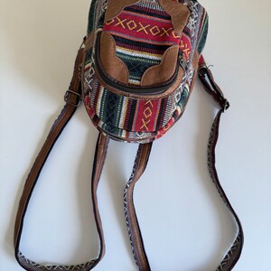 May include: A small, round, brown and multi-coloured patterned backpack with a zipped pocket on the front. The backpack has adjustable straps.