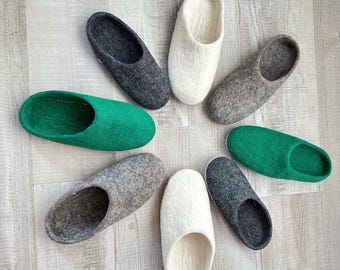 May include: Eight pairs of felt slippers in various colours, including grey, white, and green. The slippers are arranged in a circle on a light wood surface.