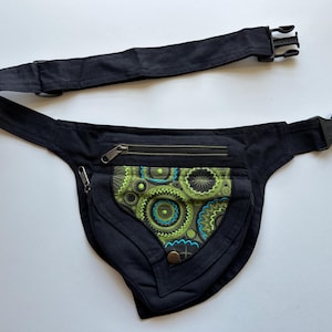 May include: Black fanny pack with a patterned front pocket. The pocket features a design with green, blue, and yellow circular shapes. The pack has a black adjustable strap with a plastic buckle and two zippered compartments.