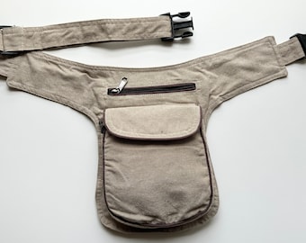May include: A beige canvas fanny pack with a brown zippered pocket and a black adjustable buckle strap.