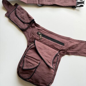 May include: A brown canvas fanny pack with multiple pockets and a zippered compartment. The pack has a long adjustable strap with a buckle closure.