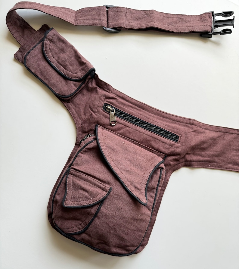 May include: A brown canvas fanny pack with multiple pockets and a zippered compartment. The pack has a long adjustable strap with a buckle closure.