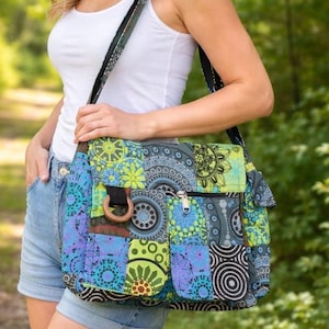 May include: A patchwork shoulder bag with a wooden ring detail. The bag features geometric and floral patterns in blue, green, and purple. It has a zippered pocket and a long strap. The bag's measurements are in centimetres.