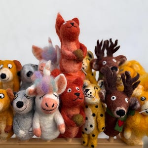 May include: A collection of handmade felt animal figurines, including a squirrel, bear, unicorn, dog, lion, and deer. The figurines are brightly colored and have detailed features. The animals are arranged together, creating a whimsical display.