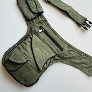 May include: A green canvas fanny pack with multiple pockets and a black adjustable strap. The pack has a zippered pocket and a large flap pocket with a black trim.