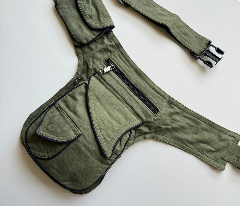 May include: A green canvas fanny pack with multiple pockets and a black adjustable strap. The pack has a zippered pocket and a large flap pocket with a black trim.
