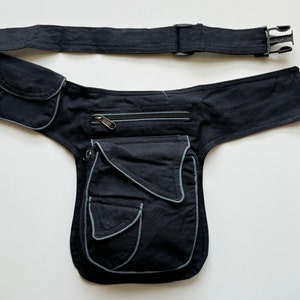 May include: Black canvas fanny pack with multiple pockets and a zippered compartment. The pack has a wide adjustable belt with a buckle closure.