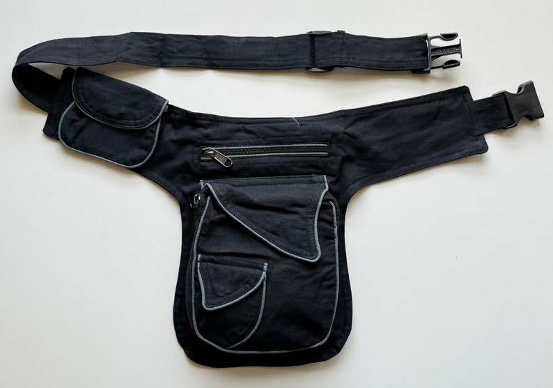 May include: Black canvas fanny pack with multiple pockets and a zippered compartment. The pack has a wide adjustable belt with a buckle closure.