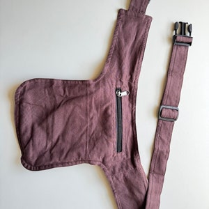 May include: A brown canvas fanny pack with a zippered pocket and adjustable strap. The strap has two black plastic buckles.