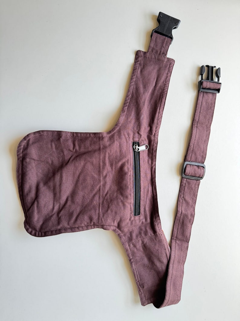 May include: A brown canvas fanny pack with a zippered pocket and adjustable strap. The strap has two black plastic buckles.