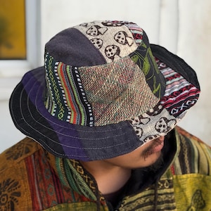 May include: A patchwork bucket hat in a mix of patterned fabrics. The hat features a wide brim and a variety of colours including purple, black, green, red, and tan. The hat has a mix of textures, including woven and printed designs. A unique accessory.
