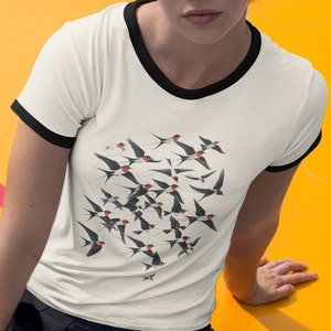 May include: A white t-shirt with a black ringer neckline features a graphic print of a flock of black and red birds in flight.