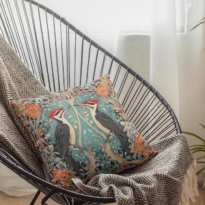 May include: A decorative throw pillow with a blue, green, and orange floral pattern featuring two black and red woodpeckers.