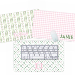 May include: Three decorative desk mats with floral and gingham patterns. One mat features a green and white floral design with the name "Brittany" in pink. Another has a pink and white gingham pattern with the name "Janie" in green. The third mat has a floral design with a keyboard.