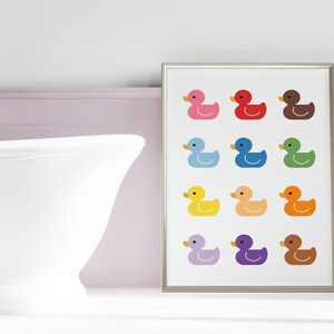 May include: A framed print with a white background and 12 colorful rubber duck illustrations. The ducks are arranged in four rows of three. Each duck is a different color, including pink, red, brown, blue, green, yellow, orange, purple, and brown.