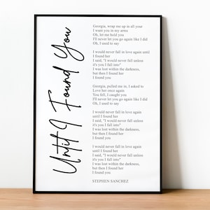 Könnte beinhalten: Gerahmter Kunstdruck mit dem Songtext "Until I Found You" von Stephen Sanchez in schwarzer Schrift auf weißem Hintergrund. Der Druck befindet sich in einem schwarzen Rahmen und liegt auf einer Holzoberfläche.