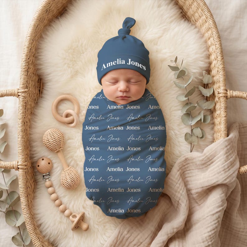 K&ouml;nnte beinhalten: Ein dunkelblaues Baby-Pucktuch und eine passende Knotenm&uuml;tze mit dem Namen Amelia Jones, der in einem sich wiederholenden Muster aus wei&szlig;en Serif- und Schreibschriften gedruckt ist. Die M&uuml;tze zeigt den Namen Amelia Jones in wei&szlig;er Serifenschrift.