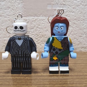 Pode incluir: Um par de brincos pendentes com minifiguras Lego de Jack Skellington e Sally do filme O Estranho Mundo de Jack. Jack está usando seu terno listrado preto e branco característico e Sally está usando seu vestido de retalhos característico.