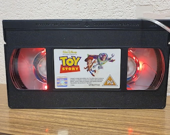 Lampada notturna/d'atmosfera a forma di videocassetta di Toy Story. Cambia colore e si controlla tramite telecomando.