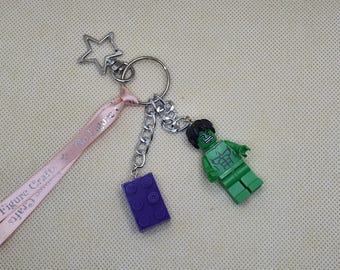 May include: A keychain featuring a green Lego Hulk figure, a purple Lego brick, and a silver star-shaped charm. The keychain includes a pink ribbon with the text "Go Figure Crafts".
