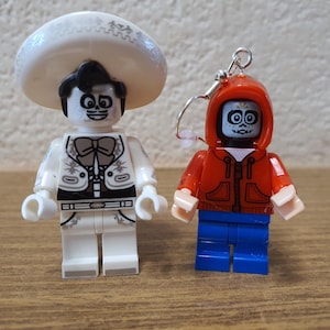 May include: Two Lego minifigures, one with a white sombrero and a white skeleton face, and the other with a red hoodie and a skeleton face.