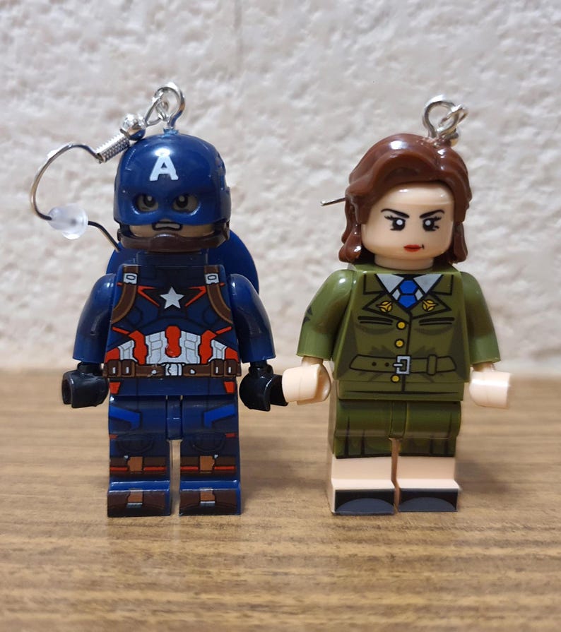 May include: A pair of Lego minifigure earrings featuring Captain America and a woman in a green military uniform. The earrings are silver and have a hook closure.