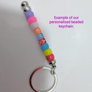 May include: A keychain featuring a silver metal ring and a vertical strand of colorful plastic beads. The beads include purple, pink, white, blue, yellow, and red, with the letters E, V, and A printed in white on the orange, blue, and red beads.