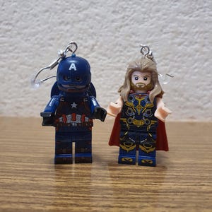 以下が含まれることがあります： キャプテン・アメリカとソーのミニチュアレゴミニフィギュアが付いたイヤリングのペア。キャプテン・アメリカは、胸に白い星が付いた、彼の特徴的な青と赤の衣装を着ています。ソーは、彼の金色の鎧と赤いマントを着ています。