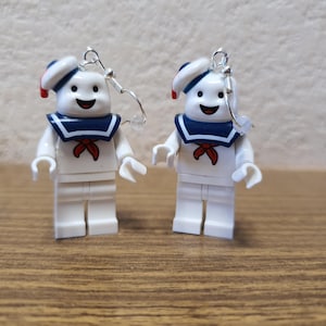 Op de afbeelding: Een paar witte Lego minifiguur oorbellen met een spookfiguur met een matrozenhoed en een rode strik. De oorbellen zijn zilverkleurig en hebben een haaksluiting.
