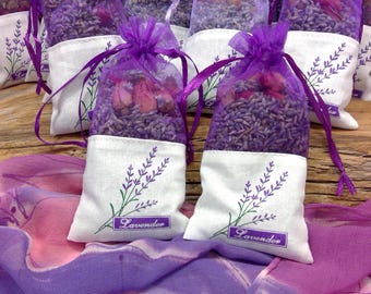 May include: Several small sachets filled with dried lavender and rosebuds. The sachets are white with a lavender sprig design and the word "Lavender" printed on them. The tops are sheer purple with a purple ribbon tie.