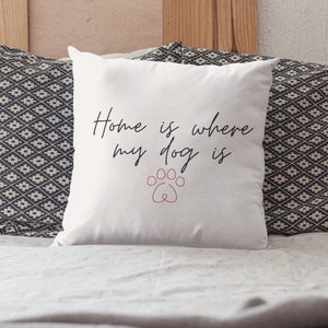 May include: White throw pillow with the text "Home is where my dog is" in black script font. A pink paw print is centered below the text.