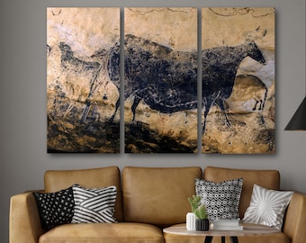 Può includere: Una stampa su tela a tre pannelli che presenta una pittura rupestre in bianco e nero di un grande animale, probabilmente un toro, con altri animali più piccoli sullo sfondo. La pittura è su una superficie rocciosa beige e marrone.