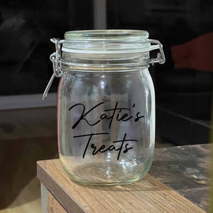 Op de afbeelding: Een glazen pot met een metalen deksel en een zwart etiket met de tekst "Katie's Treats".