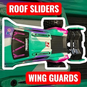 May include: A teal, white, and purple remote control car, viewed from above, with the text "ROOF SLIDERS" and "WING GUARDS" in red. The car has black tyres and the brand name "ASRMA" is visible.