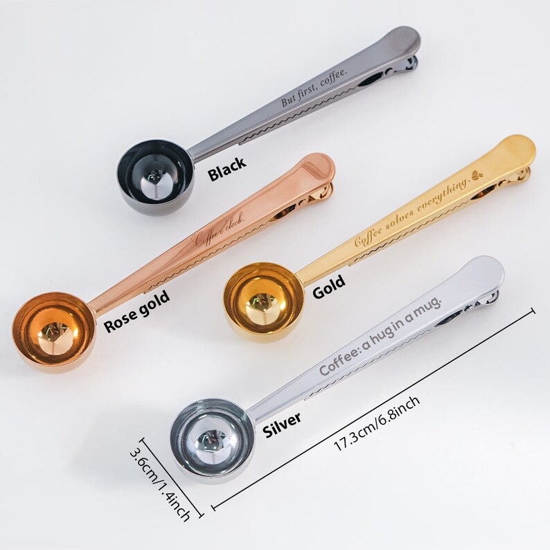 May include: Four coffee scoop clips in different colors: black, rose gold, gold, and silver. Each clip has a different engraved saying. The black clip says "But first, coffee." The rose gold clip says "Coffee Sock." The gold clip says "Coffee solves everything." The silver clip says "Coffee: a hug in a mug." The clips are 6.8 inches long and the scoops are 1.4 inches wide.