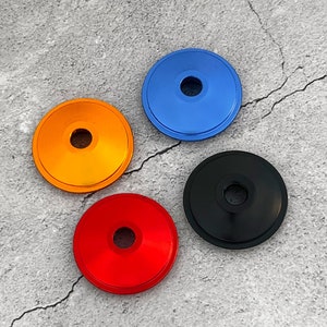 May include: Four round, metal, decorative caps in blue, orange, red, and black. The caps have a small hole in the center.