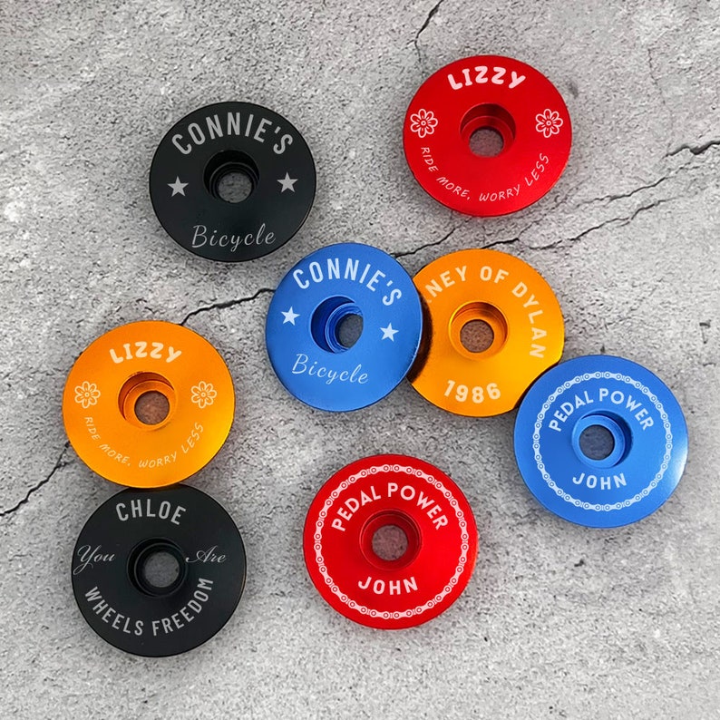 May include: Assortment of colorful bicycle stem caps with various designs and text, including "Connie's Bicycle", "Lizzy", "Ney of Dylan 1986", "Pedal Power John", and "Chloe You Are Wheels Freedom".