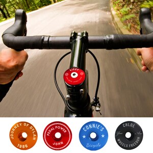 May include: A set of five colorful bicycle stem caps with different designs and text. The caps are made of metal and have a round shape. The text on the caps includes "Journey of Dylan", "Pedal Power", "Connie's Bicycle", and "Chloe You Are Wheels Freedom".