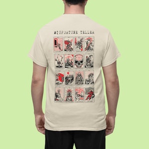 May include: Beige t-shirt featuring a tarot card design with red and black illustrations. The shirt has the text "MISFORTUNE TELLER" at the top. The tarot card images include various figures and symbols.