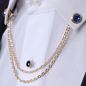 Peut inclure: Une épingle à col en chaîne dorée avec un strass bleu à une extrémité et une pierre noire à l'autre.