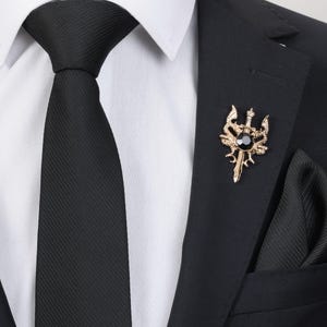 May include: A gold-toned lapel pin with a black gem in the center. The pin features a sword with a decorative design and a crown on top.