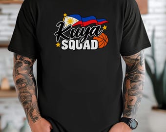 May include: A black short-sleeve t-shirt featuring a graphic print with the text Kuya SQUAD in white and black lettering. The design includes a waving Philippine flag, a basketball, and two yellow stars on a black background.
