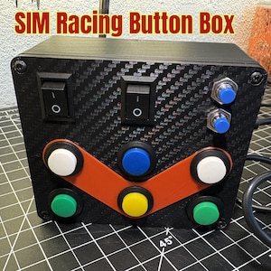May include: A black SIM Racing Button Box with a carbon fiber pattern. It features multiple buttons in various colors, including white, blue, green, and yellow, and toggle switches. The text "SIM Racing Button Box" is visible at the top.