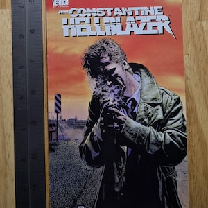 May include: A comic book cover featuring John Constantine from the Hellblazer series. The artwork depicts a man in a trench coat smoking, with the title text in bold, white letters against an orange sky. The Vertigo and DC Comics logos are visible.