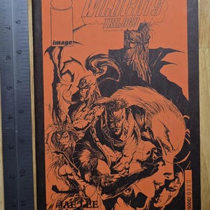 May include: A comic book cover featuring the WildC.A.T.S. Trilogy. The cover has an orange background with black illustrations of various characters. The text "WildC.A.T.S. Trilogy" and "image" are visible. The comic is numbered 0180/3000.