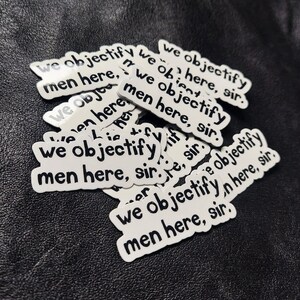 May include: A stack of white stickers with the text "We objectify men here, sir." printed in black.